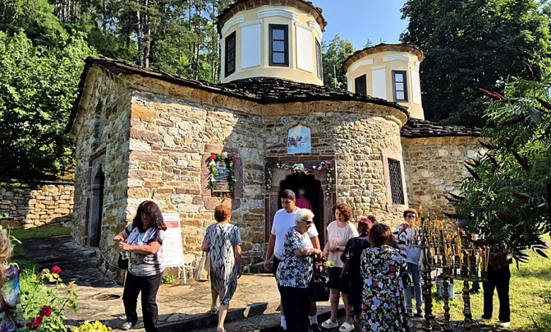 Миряни пред каменната църква на Тетевенския манастир на храмов празник, входът е украсен с цветя, до него горят свещи